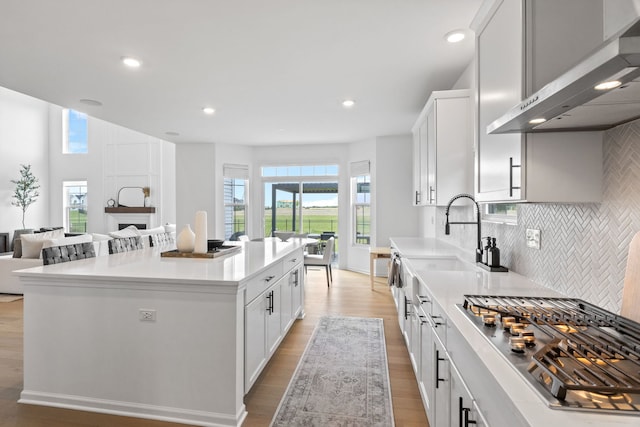 kitchen featuring wall chimney exhaust hood, stainless steel gas cooktop, light wood finished floors, recessed lighting, and tasteful backsplash
