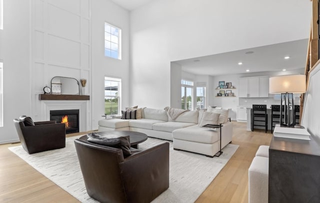 living area featuring a high ceiling, light wood finished floors, a large fireplace, and recessed lighting