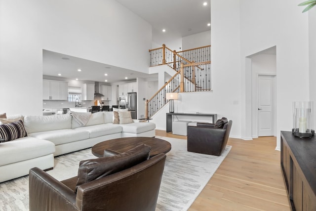 living area with a towering ceiling, stairs, light wood-type flooring, recessed lighting, and baseboards