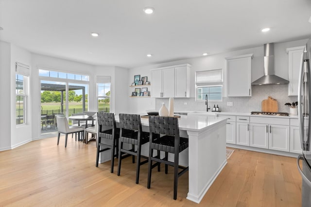 kitchen featuring wall chimney range hood, a sink, a center island, light countertops, and plenty of natural light