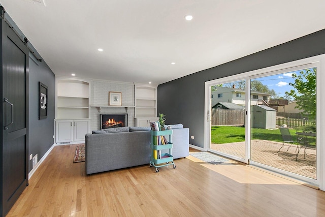 living room with light wood-style floors, baseboards, built in features, a brick fireplace, and a barn door