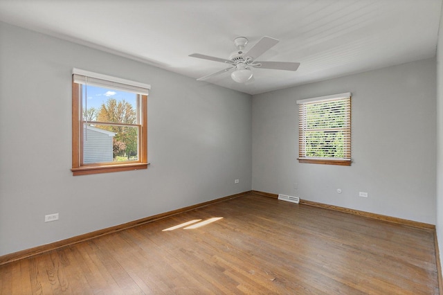 spare room featuring healthy amount of natural light, hardwood / wood-style floors, baseboards, and a ceiling fan