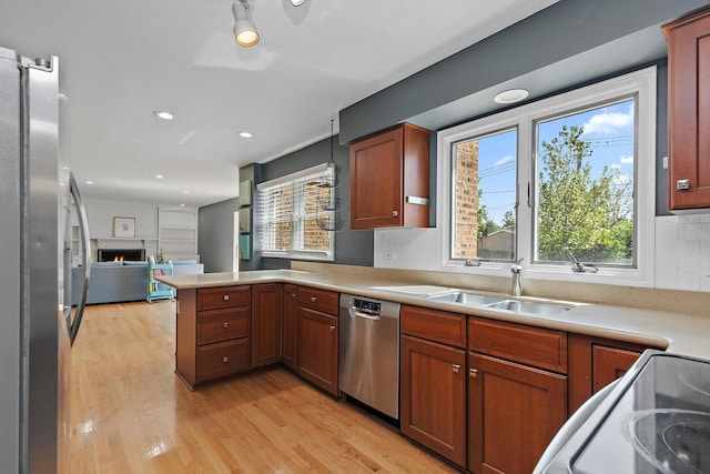 kitchen with stainless steel appliances, a sink, a peninsula, light wood-type flooring, and open floor plan