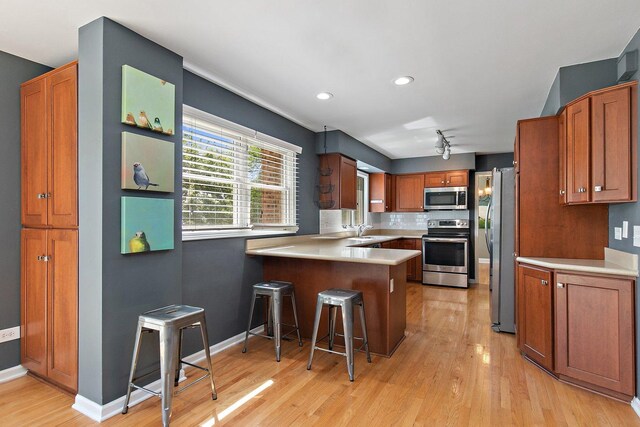 kitchen with stainless steel appliances, a peninsula, a sink, light wood-style floors, and light countertops