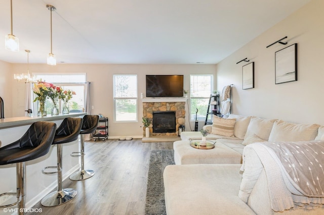 living room with wood finished floors, a stone fireplace, a chandelier, and baseboards