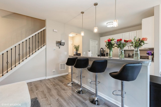 kitchen with a kitchen bar, white cabinetry, light wood finished floors, and hanging light fixtures