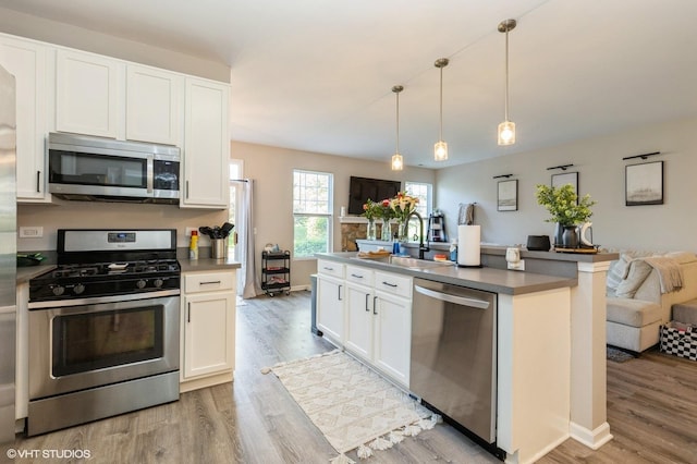 kitchen with appliances with stainless steel finishes, open floor plan, light wood-style floors, a sink, and white cabinetry