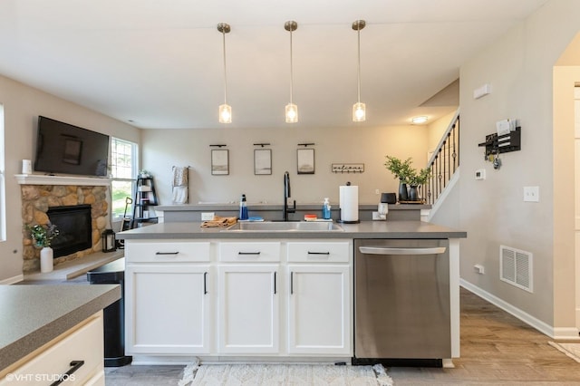 kitchen featuring stainless steel dishwasher, a sink, white cabinetry, a stone fireplace, and decorative light fixtures