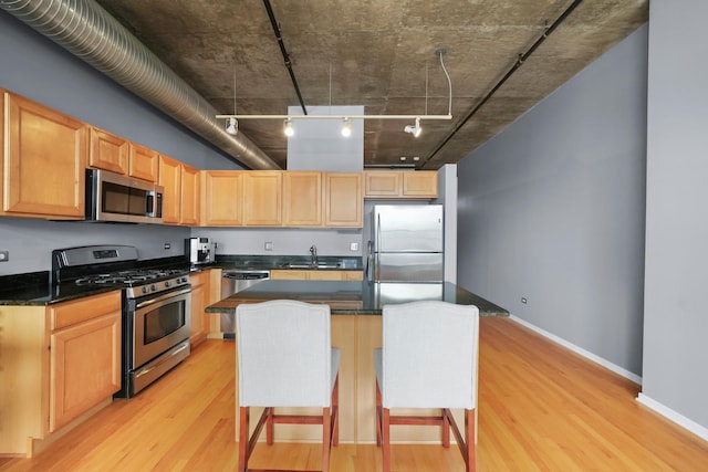 kitchen with appliances with stainless steel finishes, a sink, light wood-style floors, dark countertops, and light brown cabinets