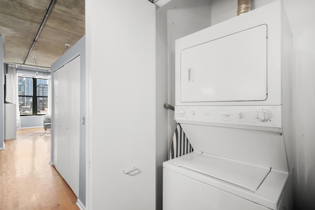 clothes washing area featuring stacked washing machine and dryer, light wood finished floors, and baseboards