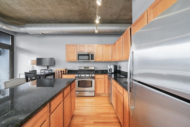 kitchen with stainless steel appliances, light wood finished floors, light brown cabinetry, and dark stone counters