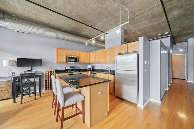 kitchen with stainless steel appliances, light brown cabinetry, light wood-style flooring, a kitchen island, and dark countertops