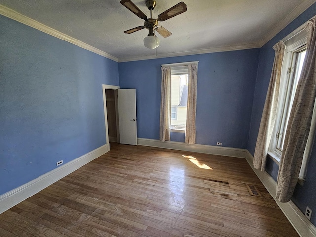 spare room featuring wood finished floors, crown molding, a ceiling fan, and baseboards