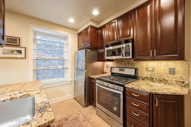 kitchen featuring appliances with stainless steel finishes, decorative backsplash, baseboards, a sink, and light stone counters