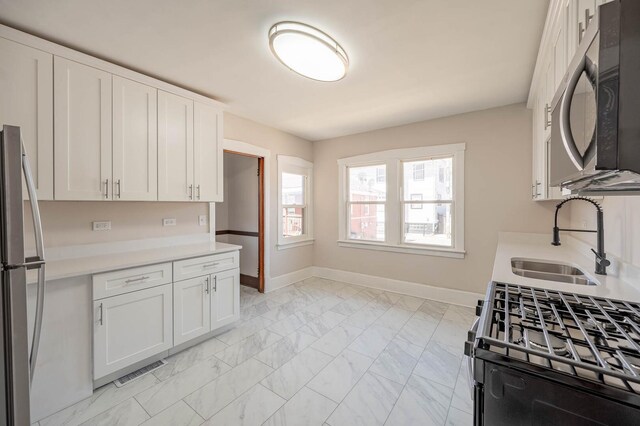 150 S 13th Ave, Maywood, IL 60153 - kitchen featuring stainless steel appliances, a sink, light marble finish flooring, baseboards, and white cabinetry