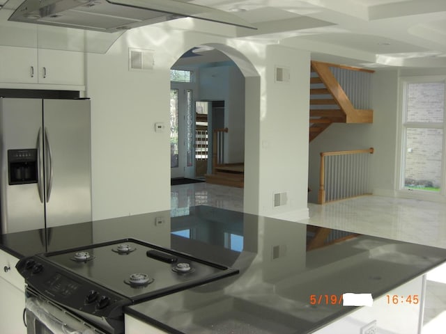 kitchen featuring stainless steel fridge, electric range oven, arched walkways, white cabinets, and dark countertops