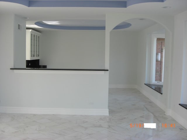 empty room featuring light marble finish floors, baseboards, and arched walkways