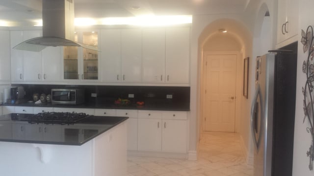 kitchen with stainless steel appliances, dark countertops, island exhaust hood, white cabinets, and glass insert cabinets