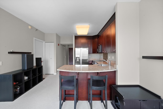 kitchen with stainless steel refrigerator with ice dispenser, a sink, light stone countertops, light carpet, and a peninsula