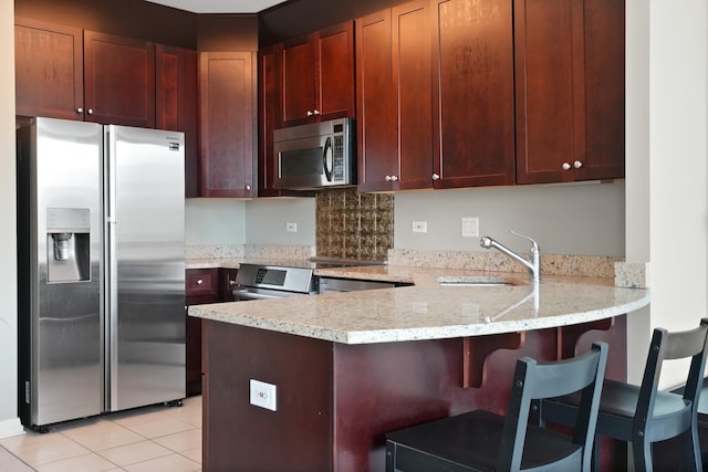 kitchen with stainless steel appliances, a sink, a peninsula, light stone counters, and light tile patterned flooring