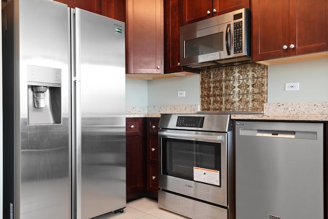 kitchen with stainless steel appliances, light stone counters, backsplash, and light tile patterned floors