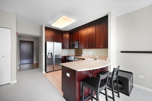 kitchen with stainless steel appliances, a sink, light countertops, a breakfast bar, and a peninsula