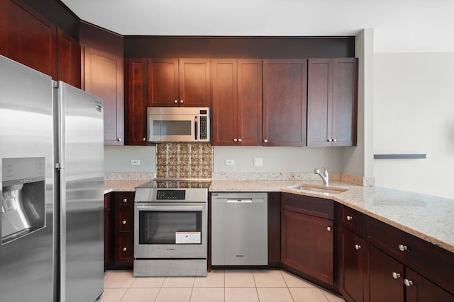 kitchen with stainless steel appliances, a sink, light stone countertops, light tile patterned floors, and reddish brown cabinets