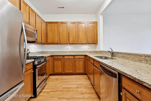 4727 N Clark St Unit 2S, Chicago, IL 60640 - kitchen featuring appliances with stainless steel finishes, brown cabinets, light wood finished floors, and light stone counters
