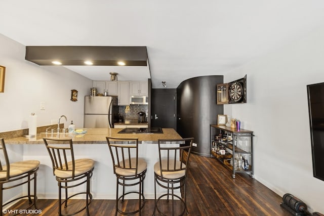 kitchen with appliances with stainless steel finishes, a peninsula, a kitchen breakfast bar, dark wood-type flooring, and tasteful backsplash