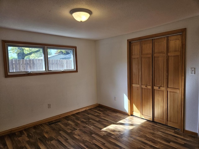 unfurnished bedroom with dark wood-style floors, baseboards, a closet, and a textured ceiling