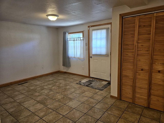 foyer entrance with a textured ceiling, baseboards, and tile patterned flooring