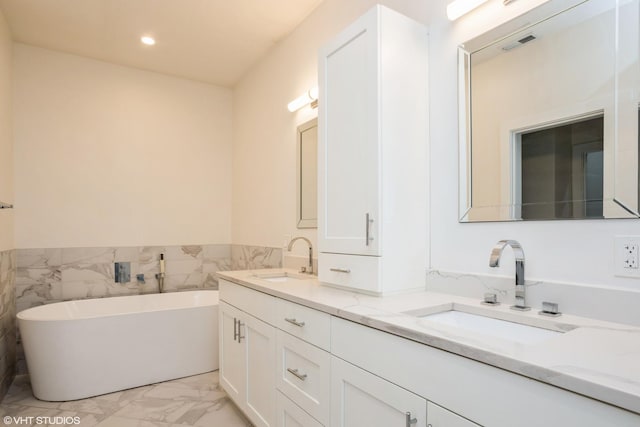 full bath with marble finish flooring, double vanity, a freestanding tub, tile walls, and recessed lighting