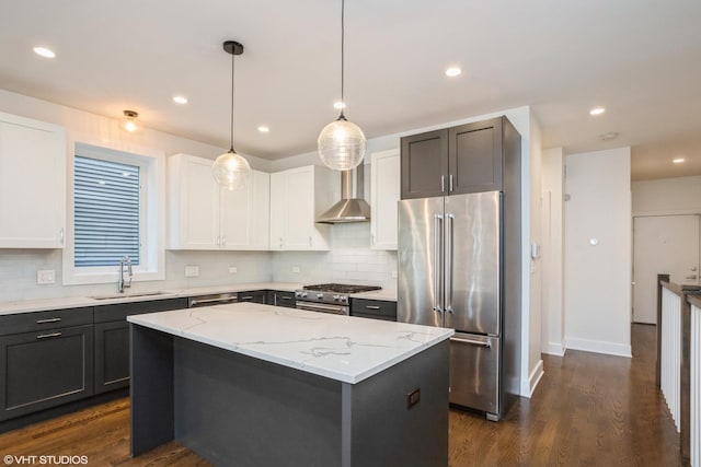 kitchen featuring high end appliances, a sink, wall chimney range hood, backsplash, and light stone counters