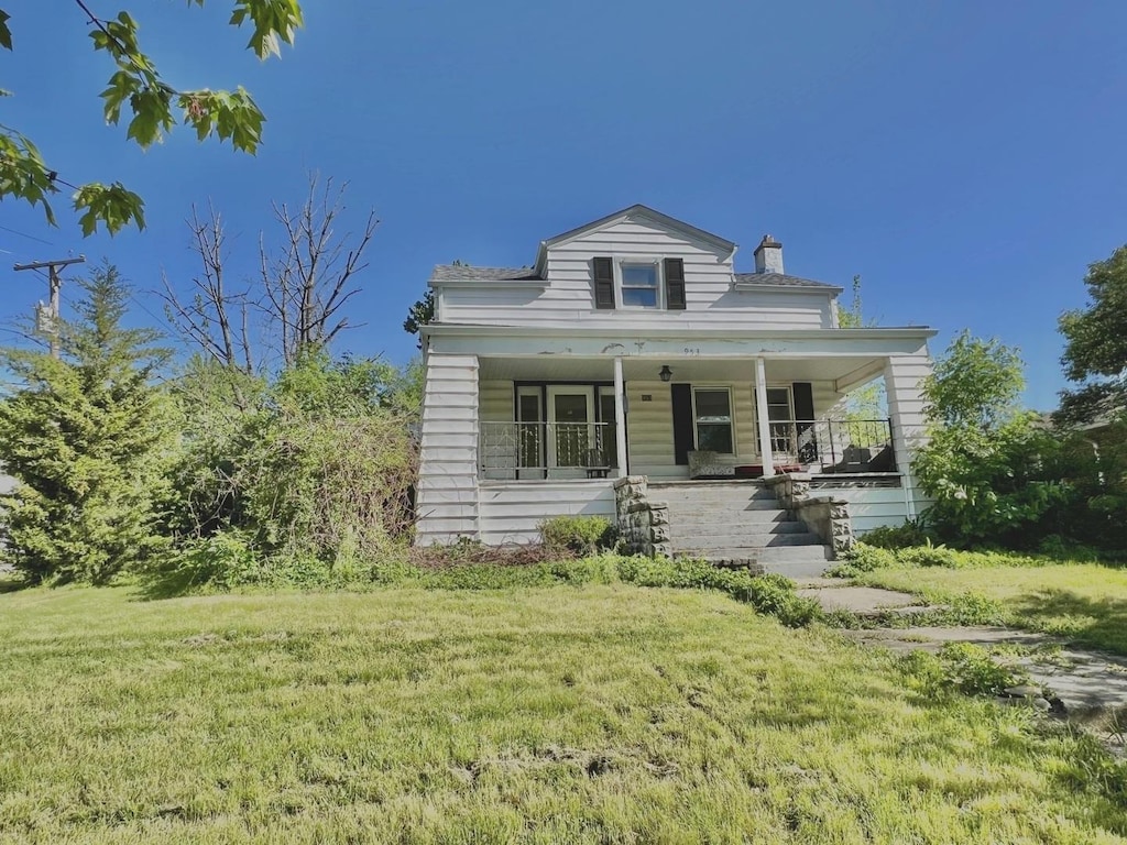 view of front facade featuring covered porch, a front yard, and a chimney