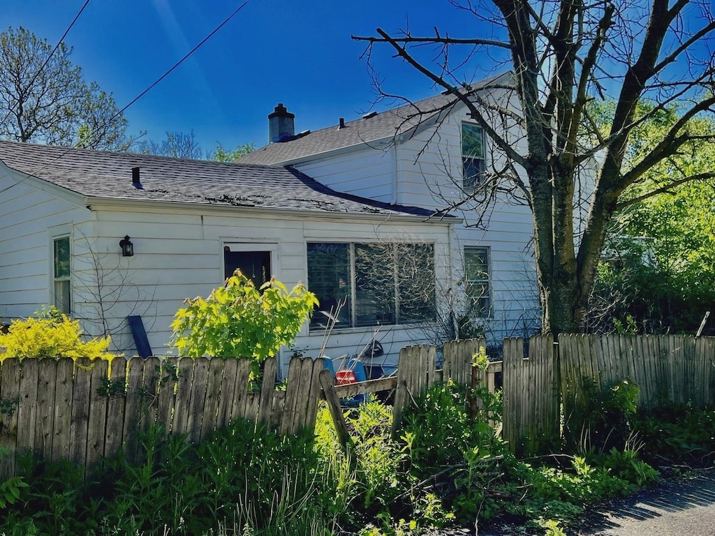 view of property exterior featuring fence, a chimney, and roof with shingles