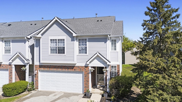 townhome / multi-family property with asphalt driveway, roof with shingles, brick siding, and a garage