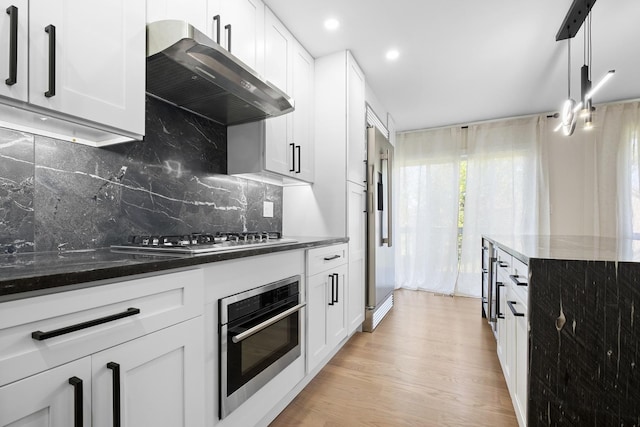 kitchen with appliances with stainless steel finishes, extractor fan, recessed lighting, dark stone counters, and light wood-type flooring