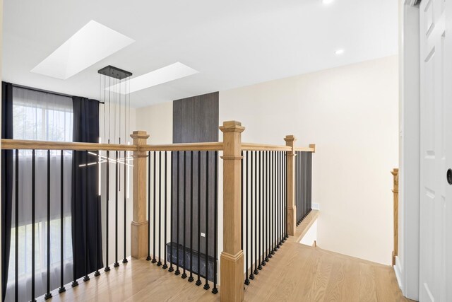 corridor with a skylight, light wood-style flooring, recessed lighting, and an upstairs landing