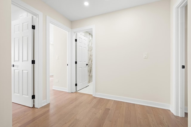 hallway featuring baseboards, light wood finished floors, and recessed lighting
