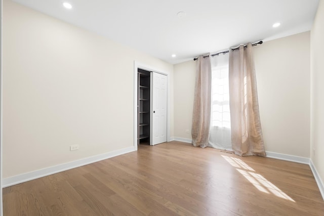 unfurnished bedroom with wood finished floors, baseboards, recessed lighting, and a closet