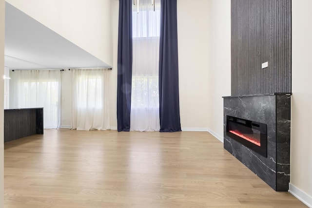 unfurnished living room with a glass covered fireplace, wood finished floors, baseboards, and a towering ceiling