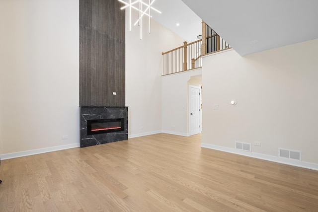 unfurnished living room with a towering ceiling, a high end fireplace, light wood-type flooring, and baseboards