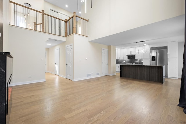 unfurnished living room with a towering ceiling, light wood-style floors, and baseboards