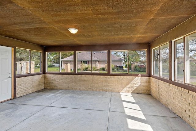 unfurnished sunroom with brick wall, concrete flooring, healthy amount of natural light, and wooden ceiling