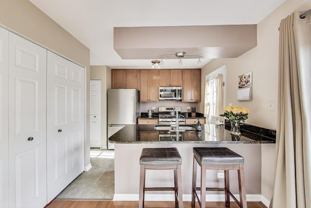 1479 N Denton Ave, Palatine, IL 60067 - kitchen featuring stainless steel appliances, a sink, brown cabinetry, dark stone countertops, and a breakfast bar area