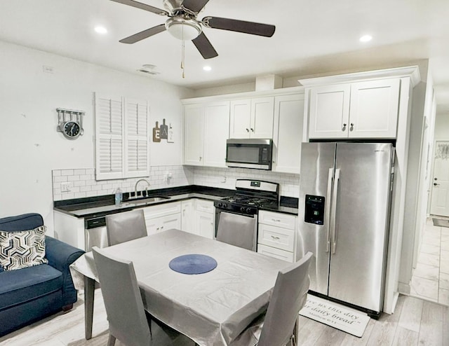 kitchen featuring appliances with stainless steel finishes, a sink, ceiling fan, dark countertops, and backsplash