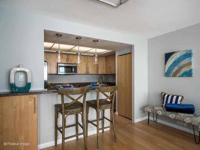 155 N Harbor Dr Unit 2011, Chicago, IL 60601 - kitchen with stainless steel microwave, brown cabinets, light wood-style floors, a kitchen bar, and pendant lighting