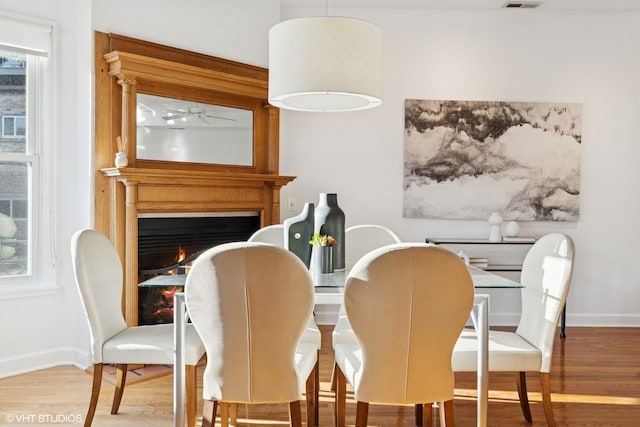 dining space featuring wood finished floors, baseboards, and a lit fireplace