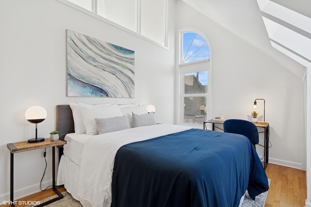 bedroom featuring a skylight, light wood finished floors, baseboards, and lofted ceiling