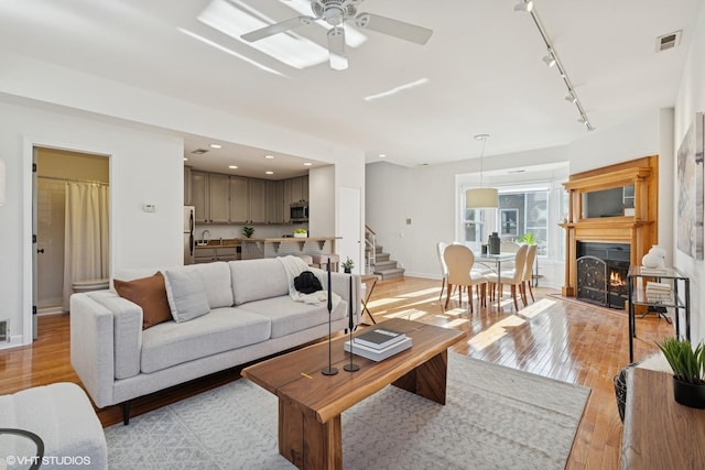 living area featuring stairway, light wood finished floors, a ceiling fan, track lighting, and baseboards